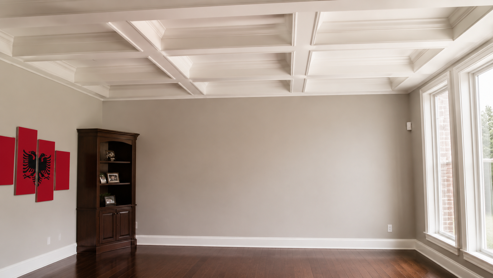 Bright empty living room with coffered ceiling, beige walls, dark wood floor, red wall art, and large windows