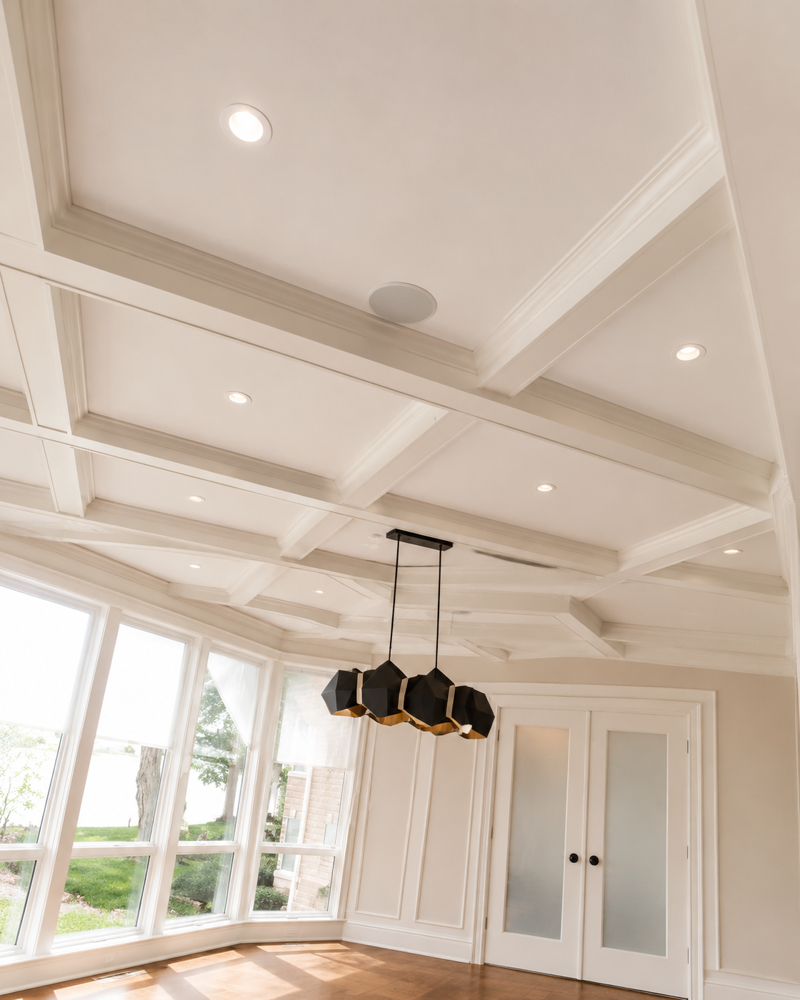 Bright modern room with white coffered ceiling, pendant lights, large windows, and double doors