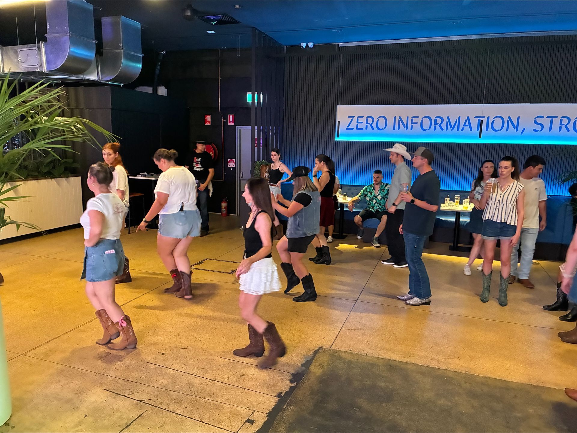 People line dancing in a room with a blue wall, wearing cowboy boots.