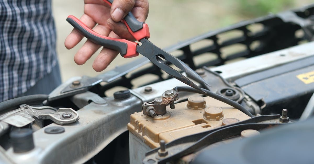 A man is holding a pair of pliers over a car battery.  | Pope Automotive