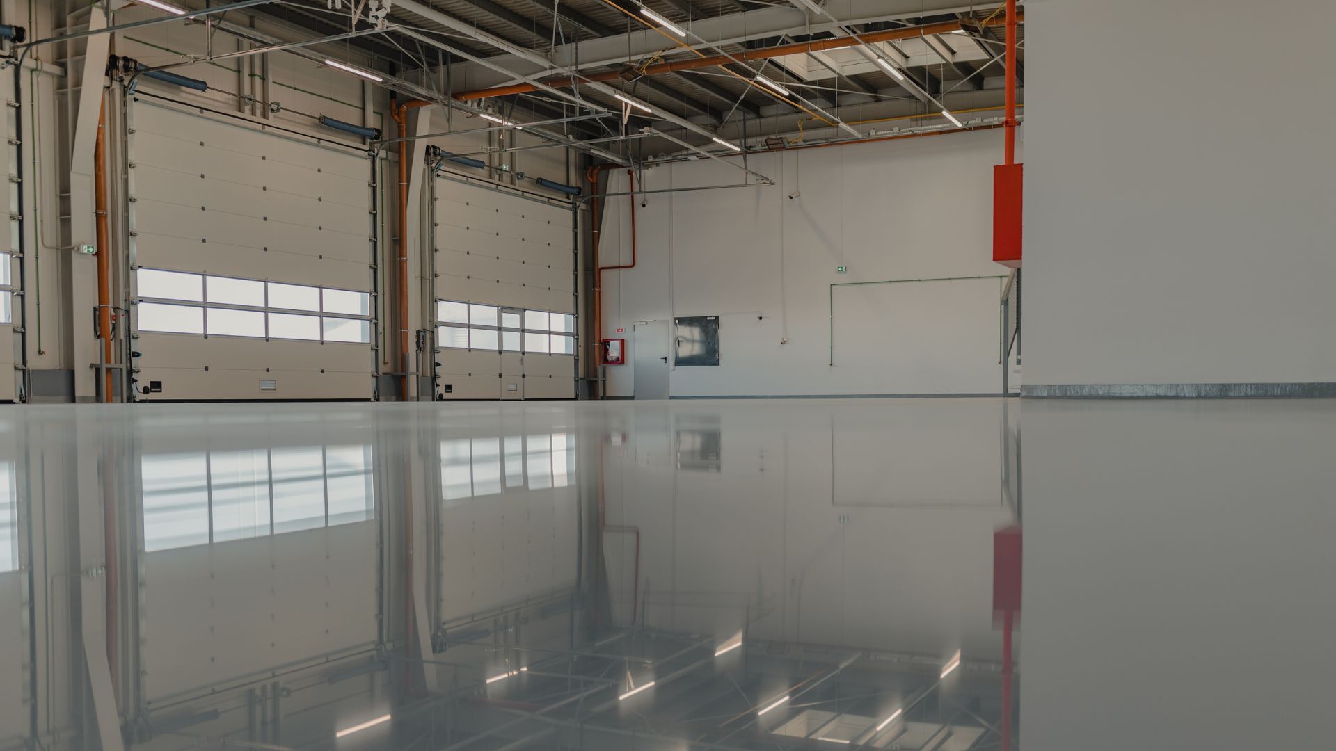 Empty warehouse with shiny concrete floor, tall yellow support beams, and boxes of goods.