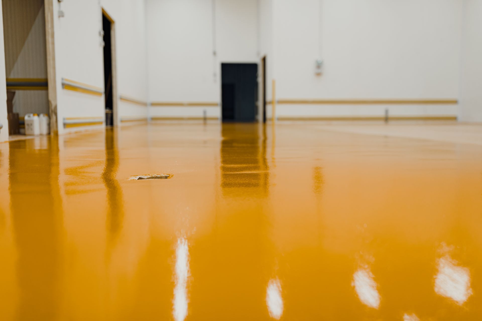 Orange epoxy floor reflecting white walls and doorways in a brightly lit room.