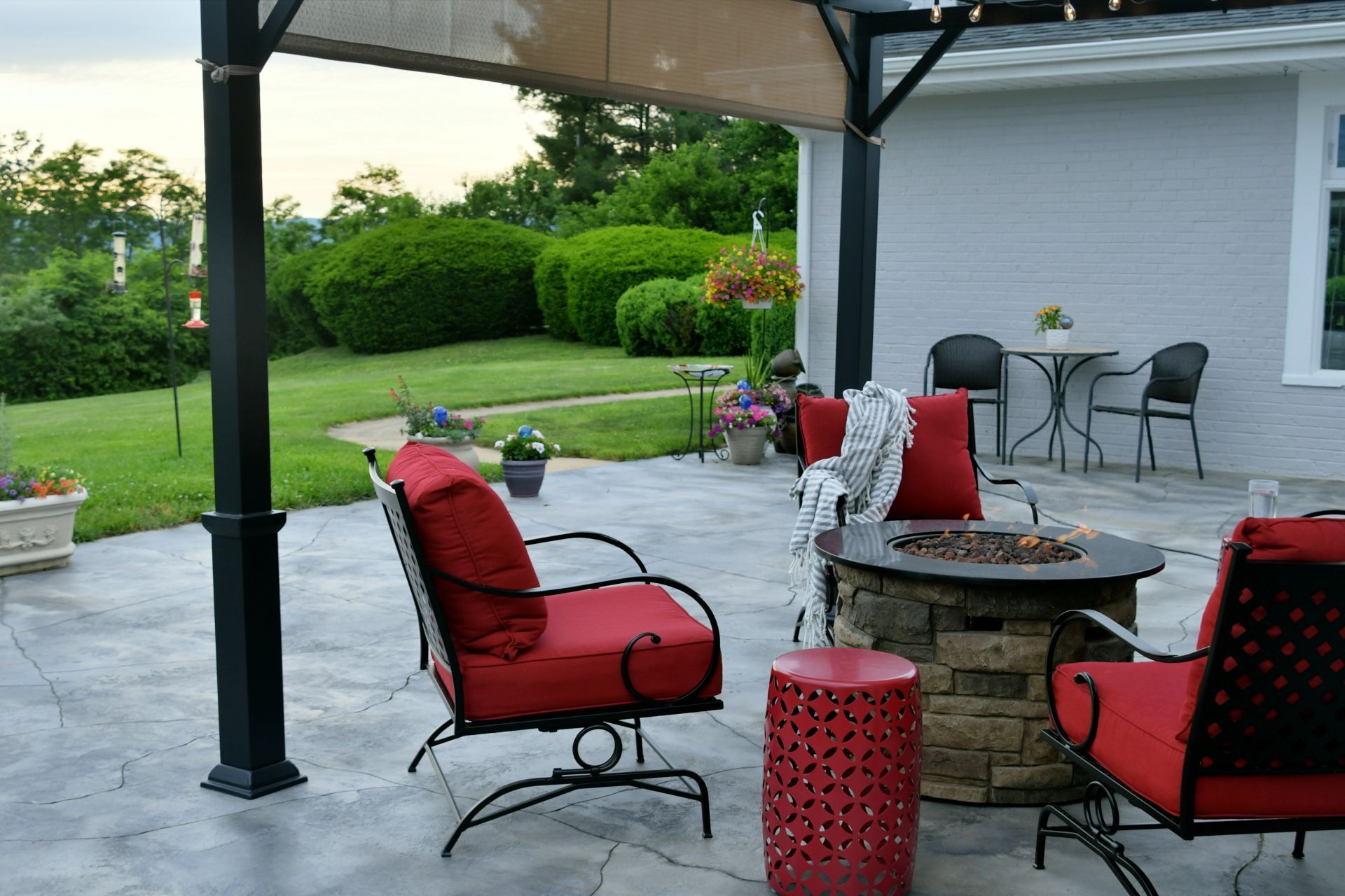 Patio with red seating, fire pit, and garden view under a pergola.