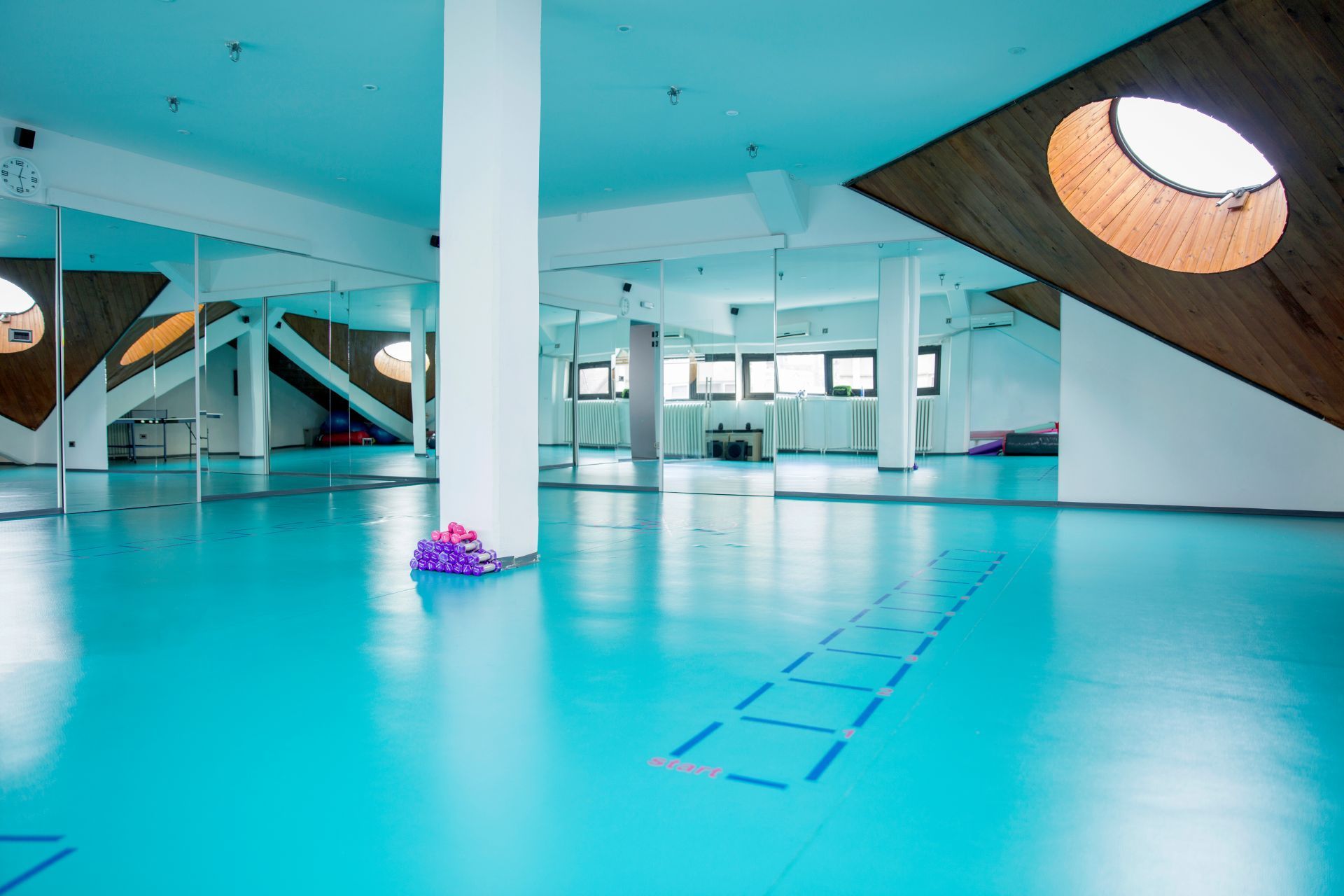 Bright turquoise dance studio with mirrors, a central pillar, and a wooden skylight.