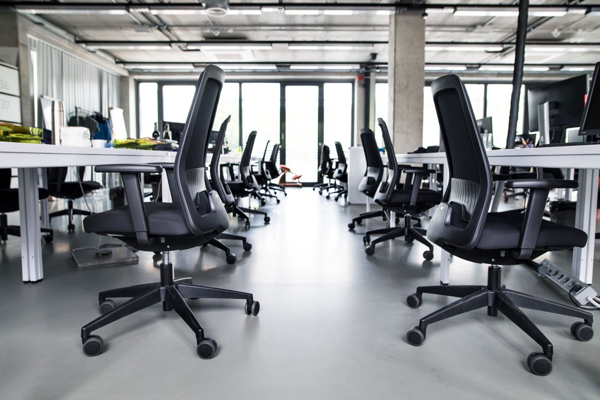 Empty modern office with rows of desks and black ergonomic chairs.