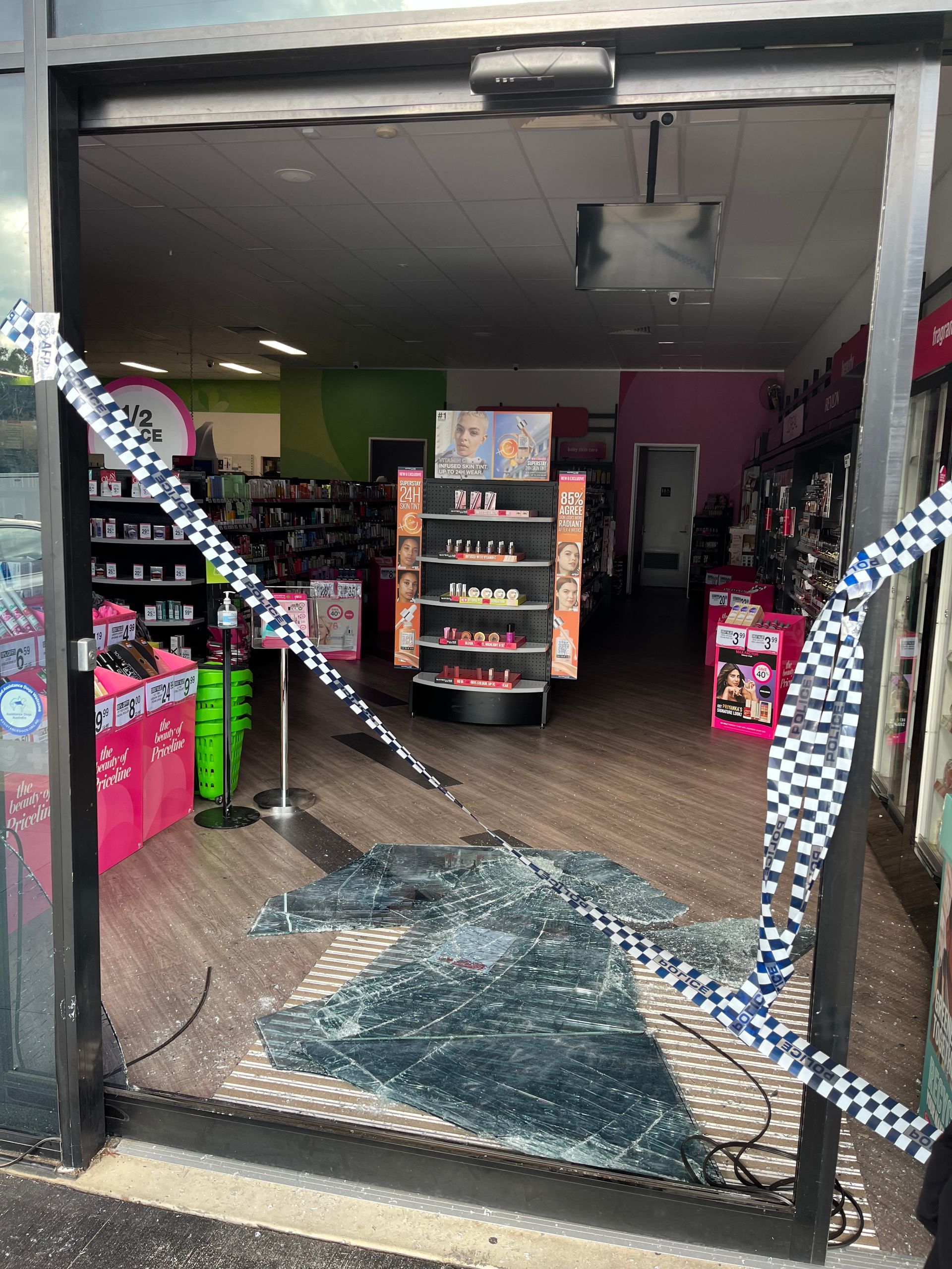 Shattered store front with police tape. Interior visible with shelves of products.