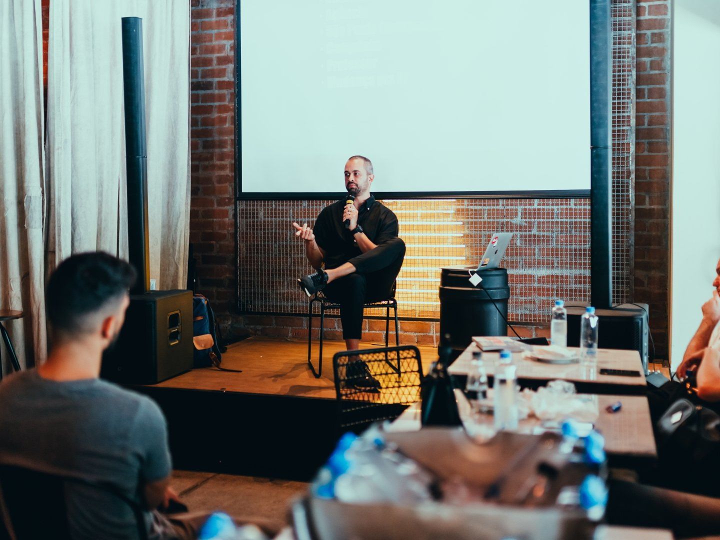 A man is sitting on a stage giving a presentation to a group of people.