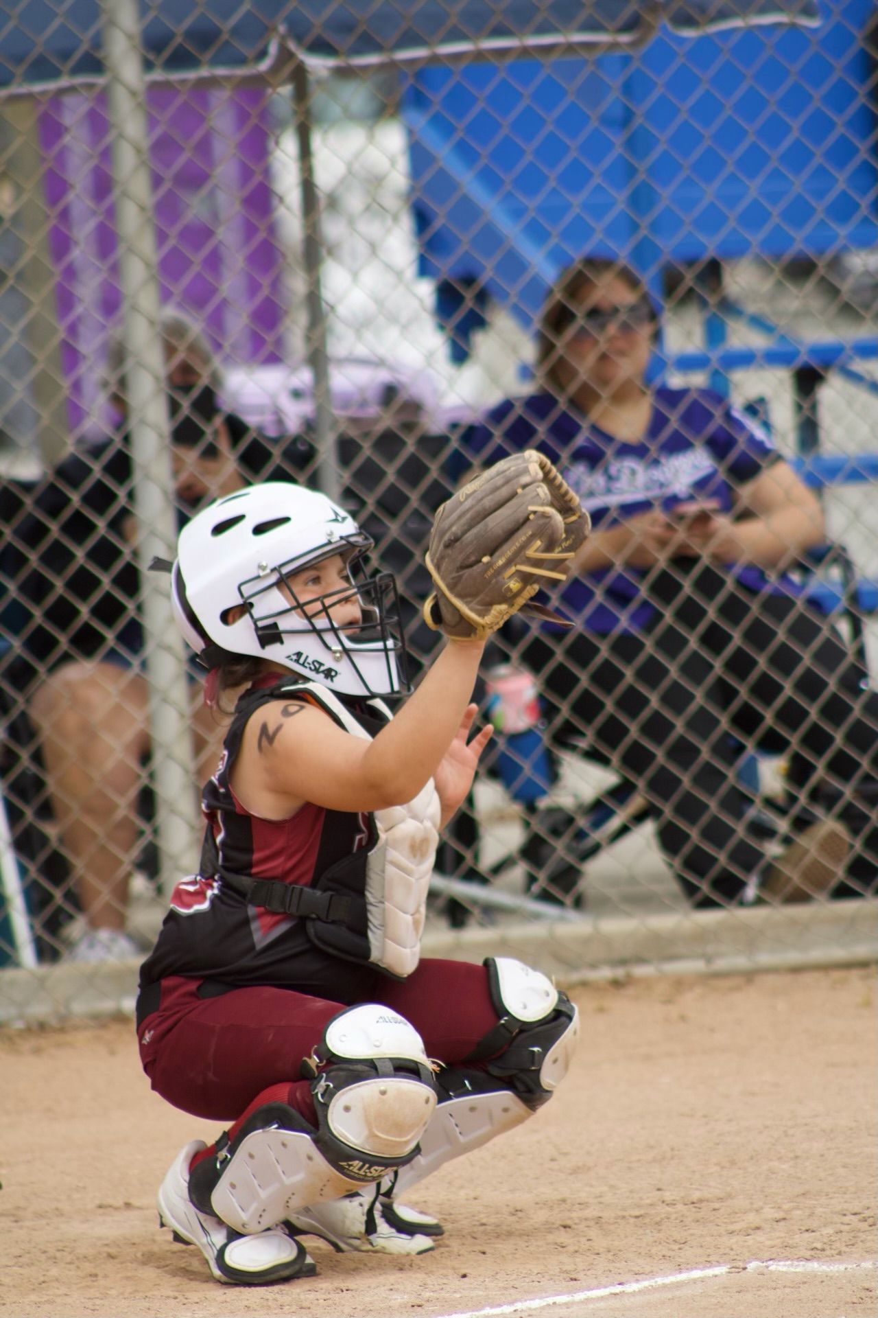 Blue helmet, softball mitt, yellow softball, and a bat on a metal bench at a softball field.