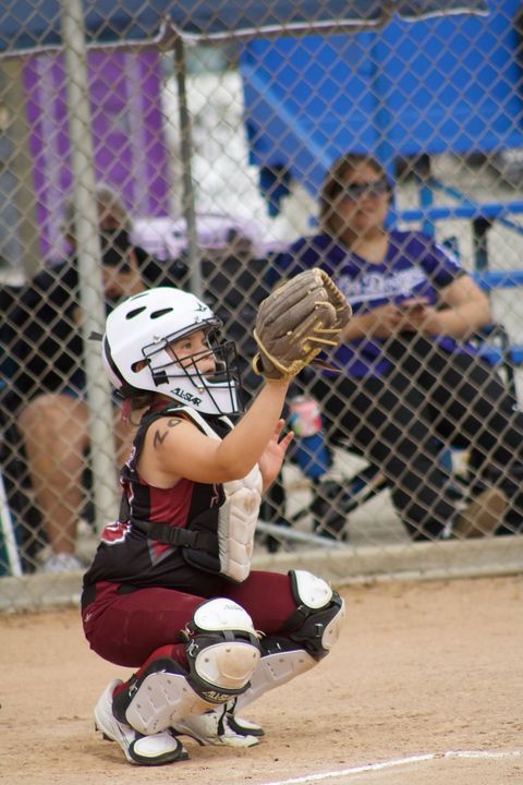 Blue helmet, softball mitt, yellow softball, and a bat on a metal bench at a softball field.