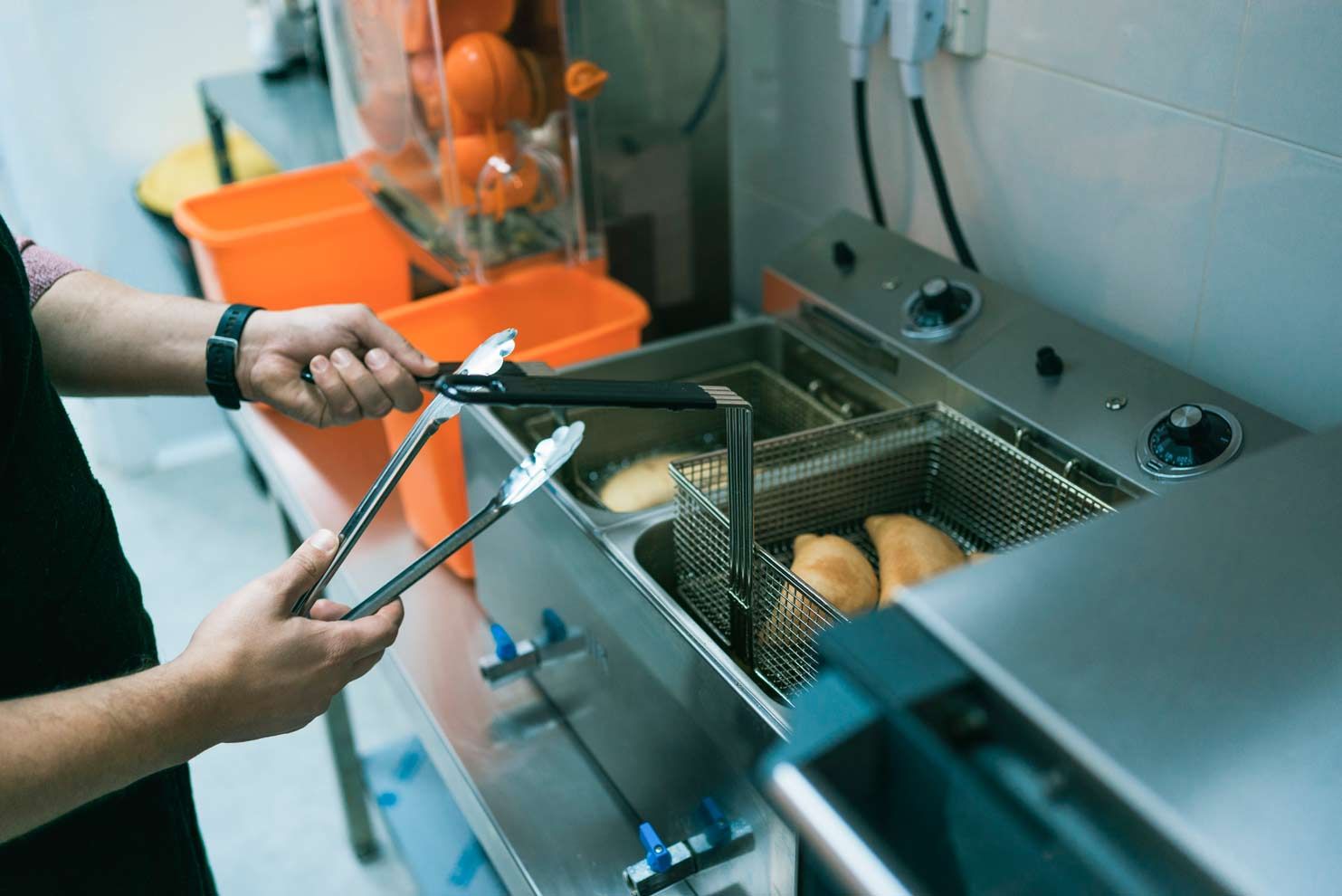 Person uses tongs to fry food in basket at a commercial kitchen.