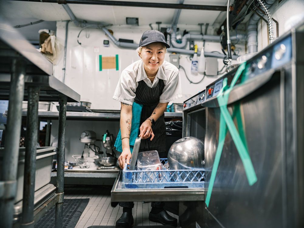 Female washing dishes using commercial food equipment in a modern restaurant kitchen.
