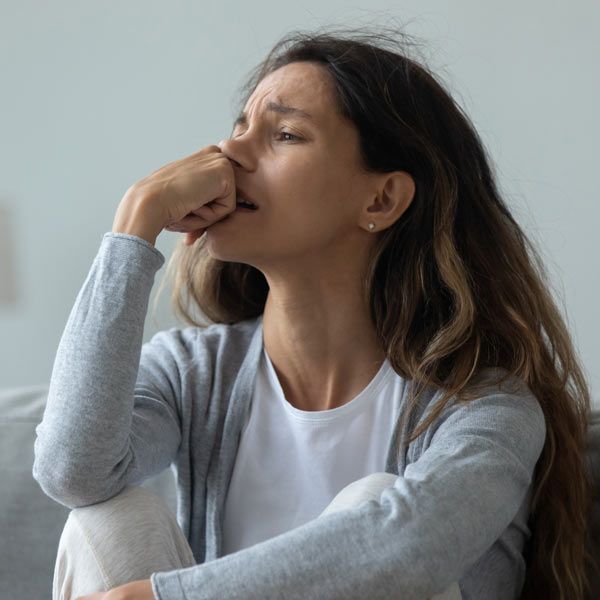 A person with long hair experiencing anxiety, with a hand over their mouth while sitting indoors.
