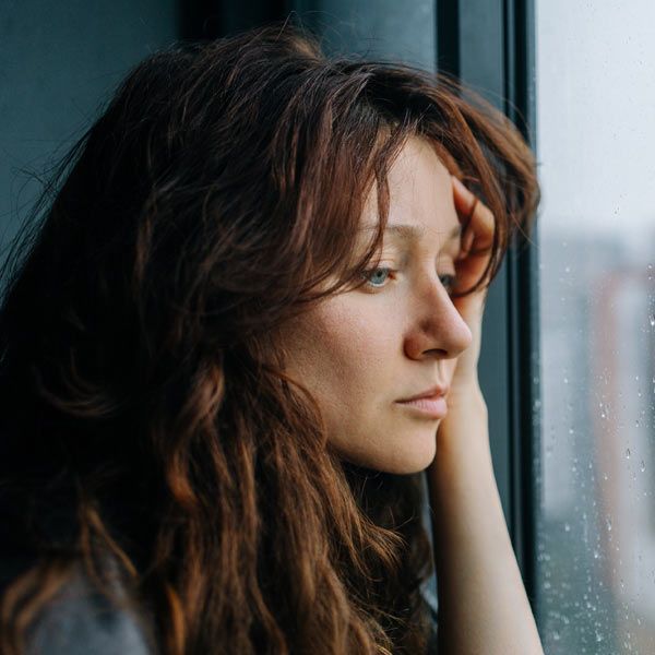Woman with depression looking out the window with a sad expression