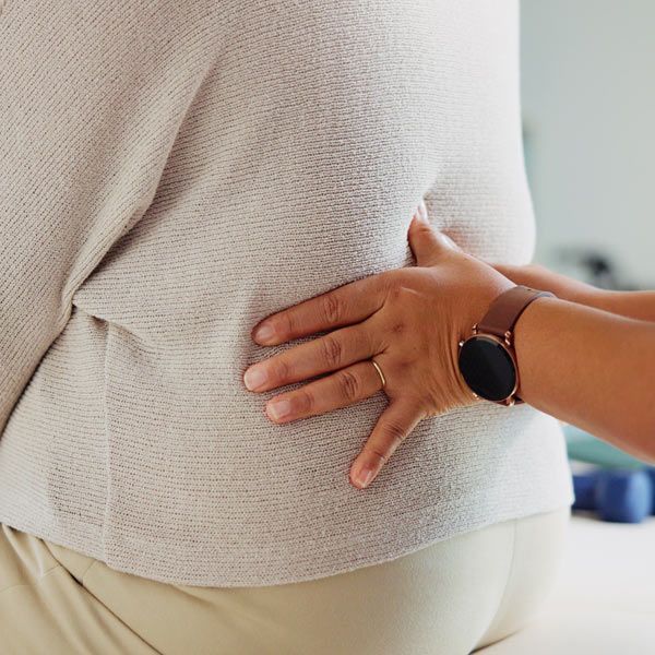 A person’s hand examines another person’s lower back pain in a professional, clinical setting.