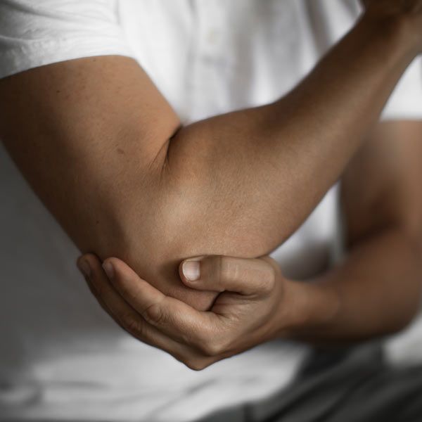 A person in a white shirt holding their bent elbow with their opposite hand, suggesting pain or discomfort.