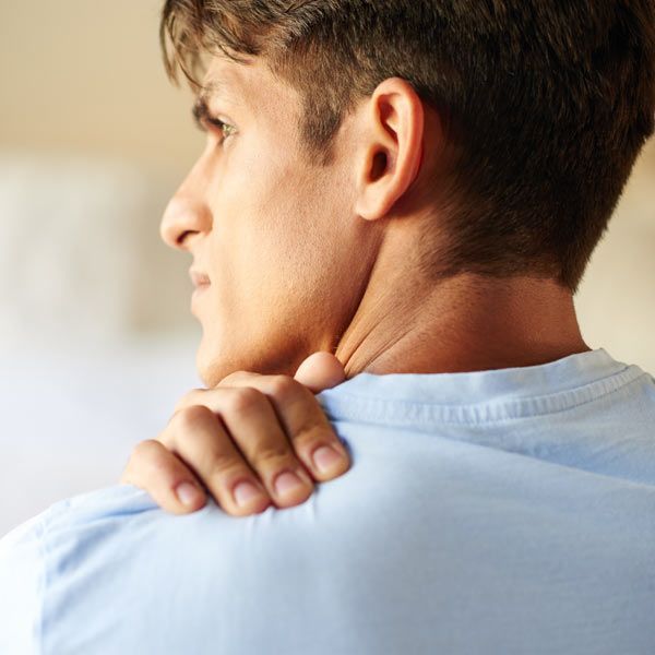 Person in a light blue shirt looking away while holding their shoulder, indicating pain or discomfort.