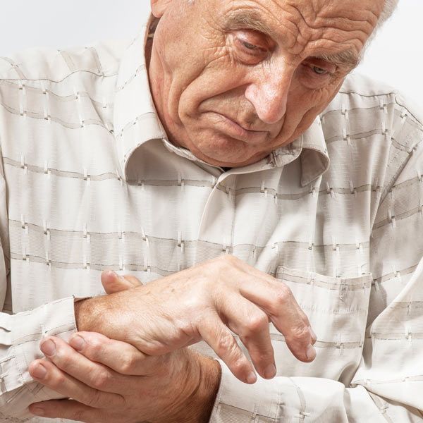 A person in a patterned shirt looking down while holding their wrist and hand, appearing to be in pain.