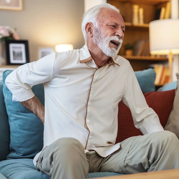 A man with a Herniated Disc sits on a sofa, clutching their lower back with a pained expression.
