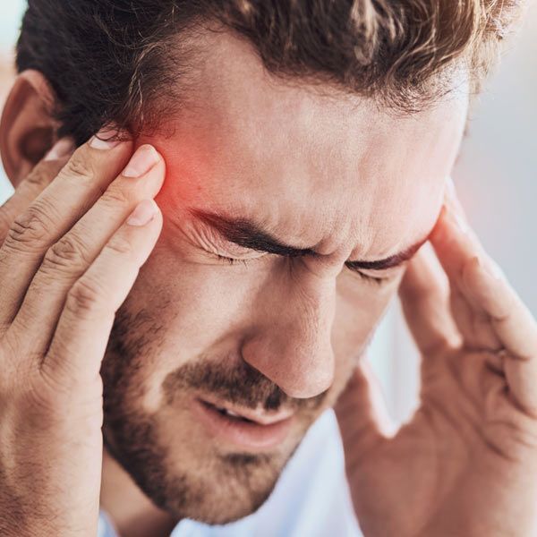 A man holds his temples with both hands, eyes closed, appearing to be in pain from a migraine.