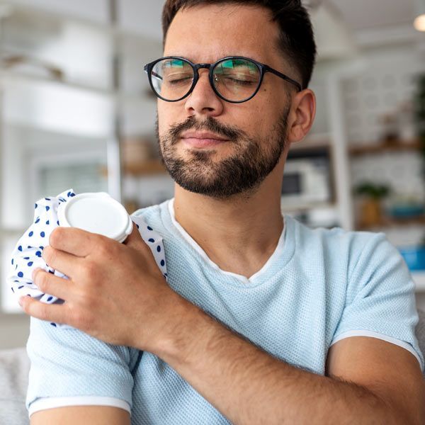 A person with a Rotator Cuff injury eyes closed holds an ice pack against their shoulder, appearing to relieve pain in a home setting.
