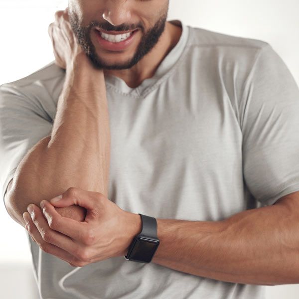 A person with Bursitis is wearing a light grey shirt and a black smartwatch, holding their elbow with one hand while touching their neck.