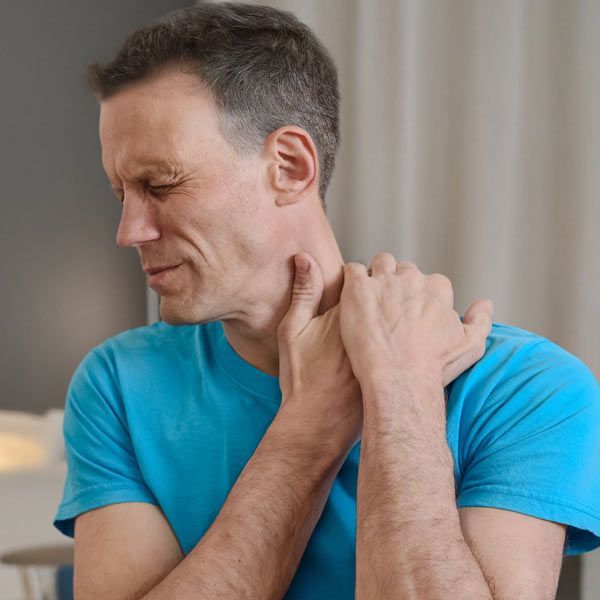 A with a Pinched Nerve is wearing a blue shirt wincing in discomfort while holding their neck with their hands.