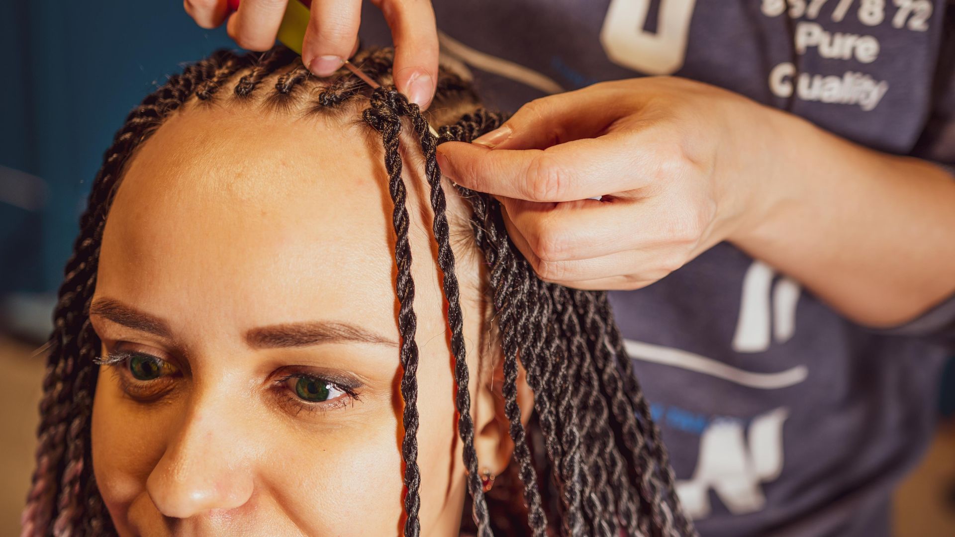 Hands braiding a person's hair into twists. Close-up with brown skin, indoors.
