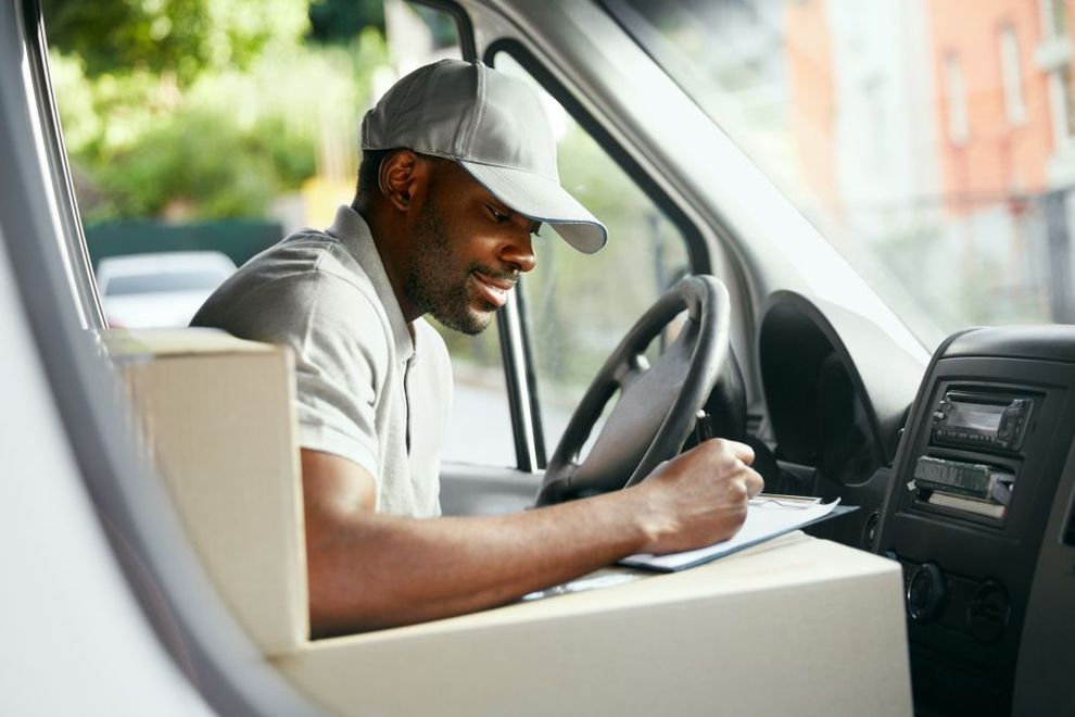 A delivery man is sitting in a van writing on a clipboard.