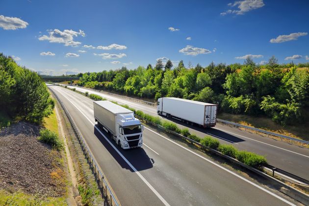 Two semi trucks are driving down a highway surrounded by trees.