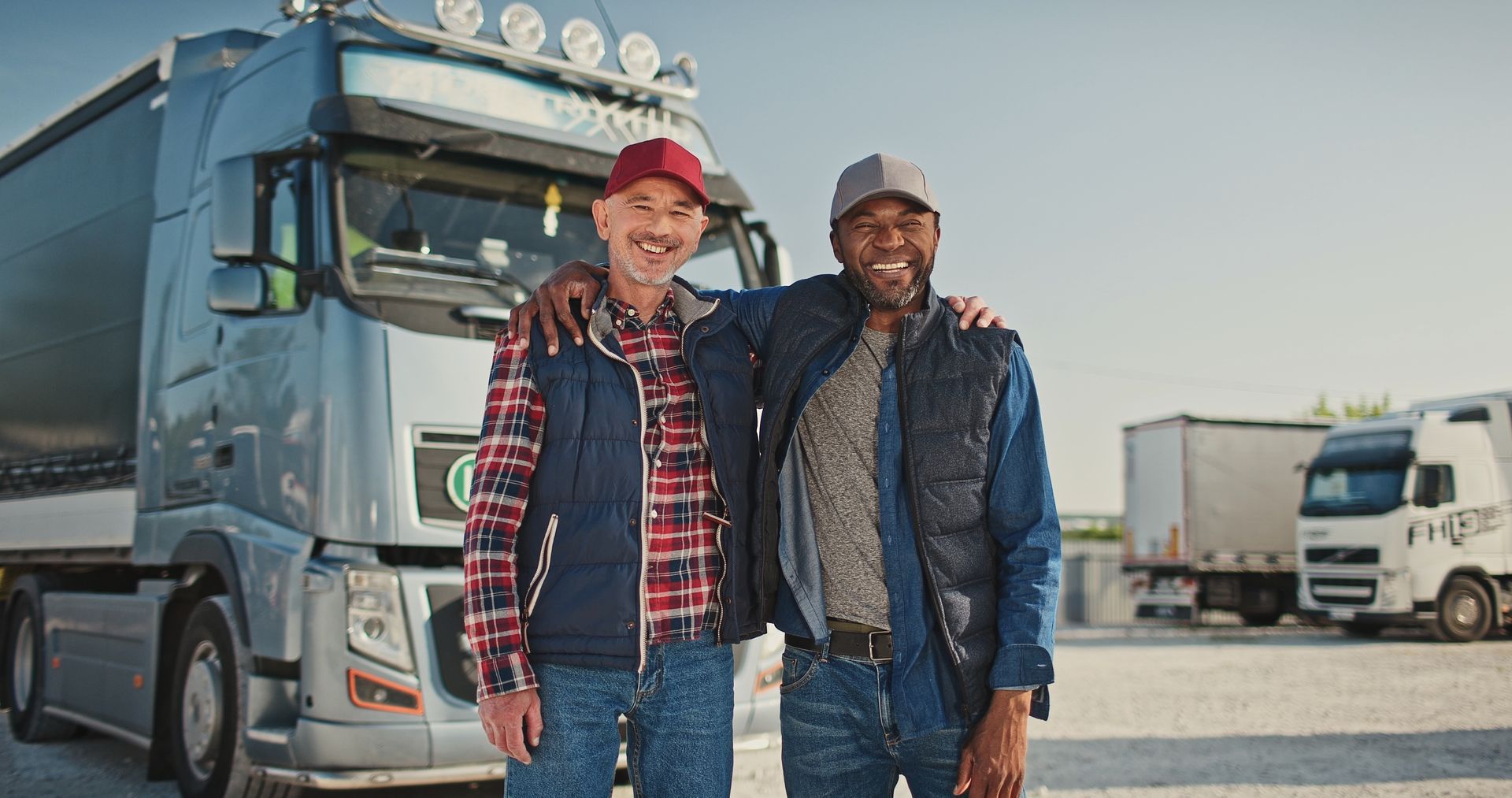 Two truck drivers are posing for a picture in front of a truck.