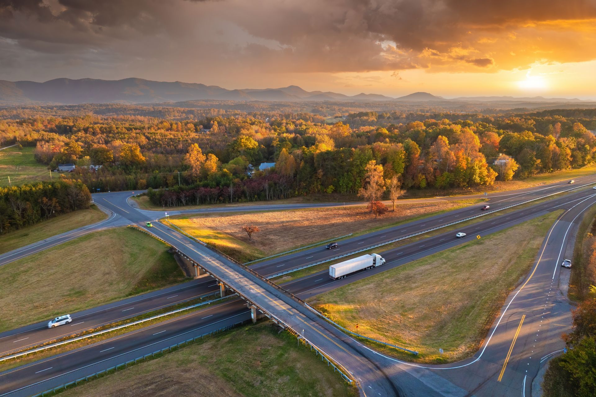 An aerial view of a highway at sunset with a truck driving down it.