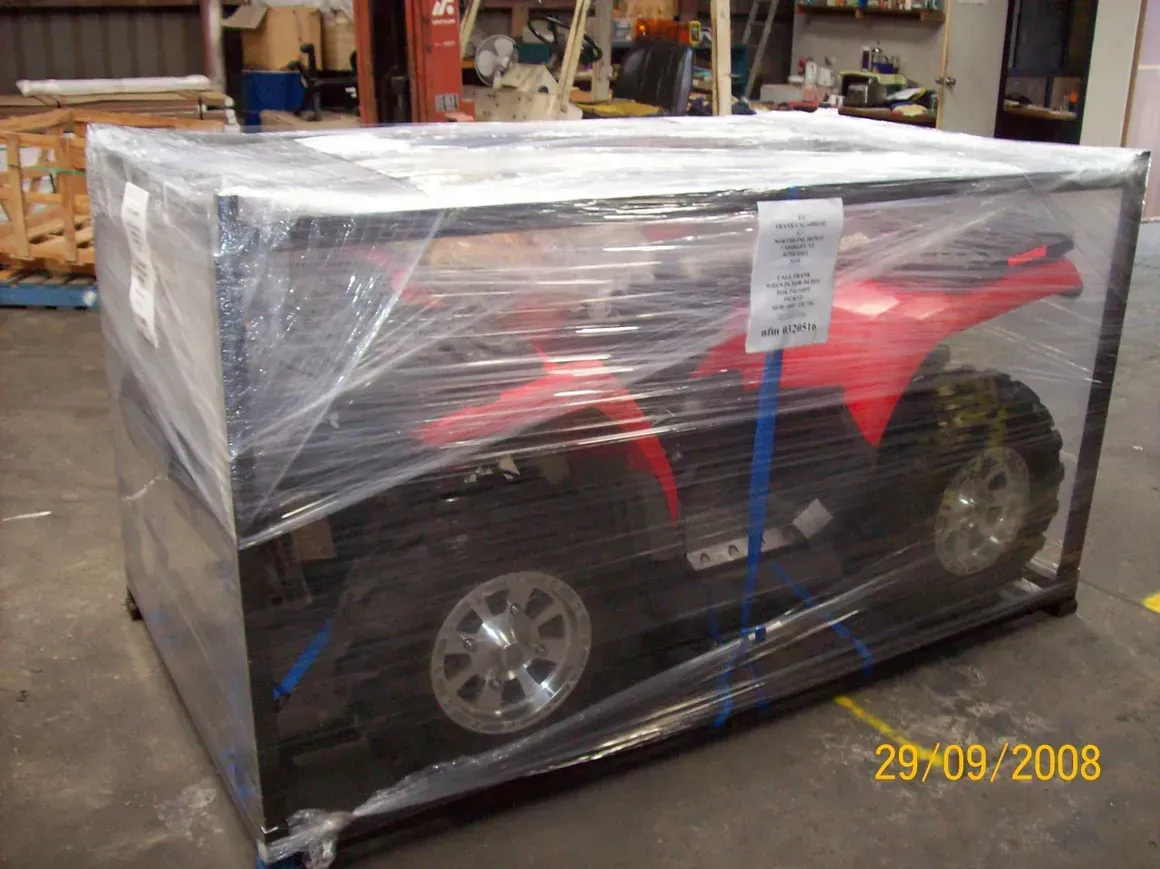 A Red ATV Is Wrapped In Plastic In A Crate — Motorcycle Transporters In Manunda, QLD