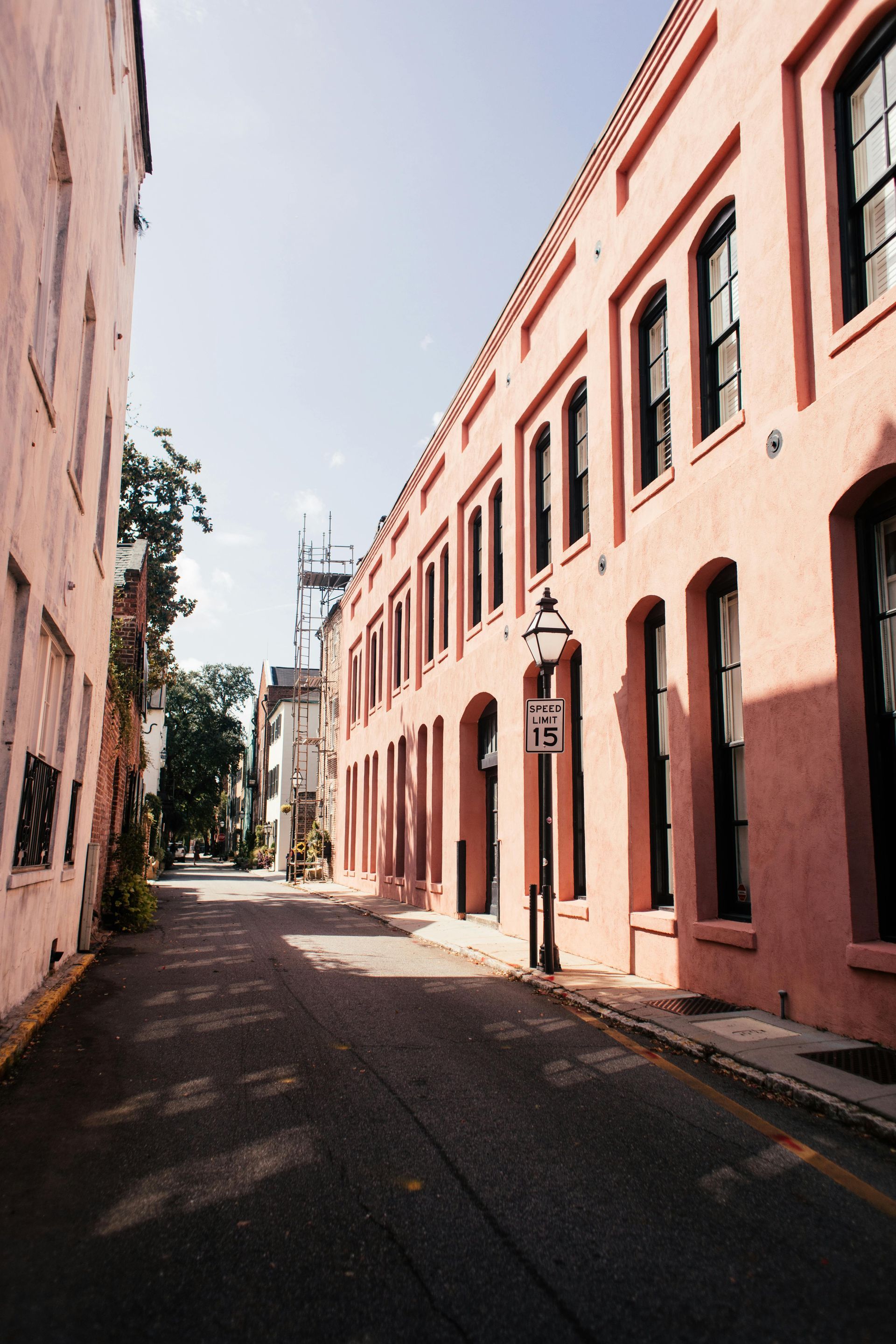 Pink buildings line a narrow street under a bright blue sky. Charleston, South Carolina.