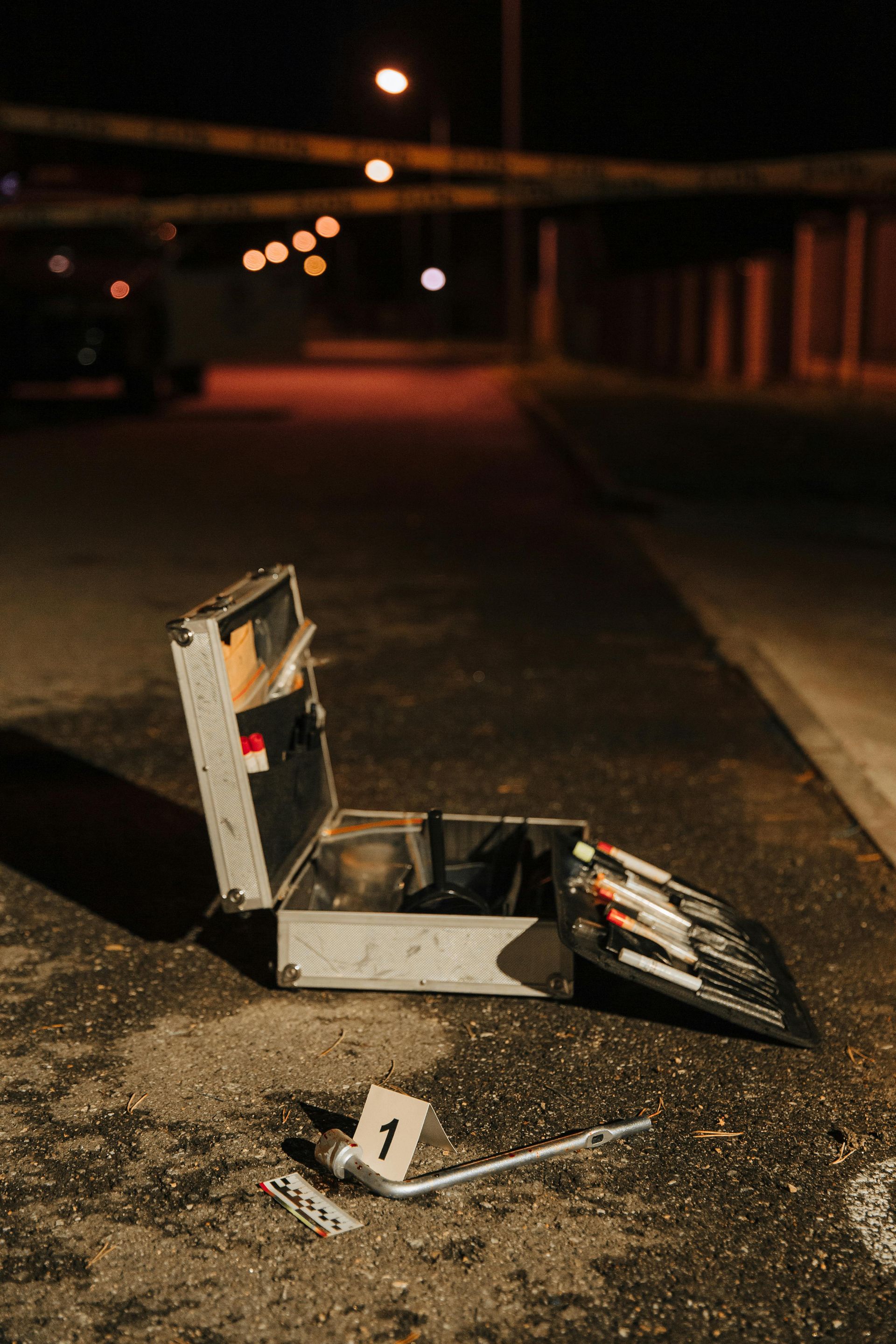 Open toolbox on pavement at crime scene, marked evidence. Night setting.
