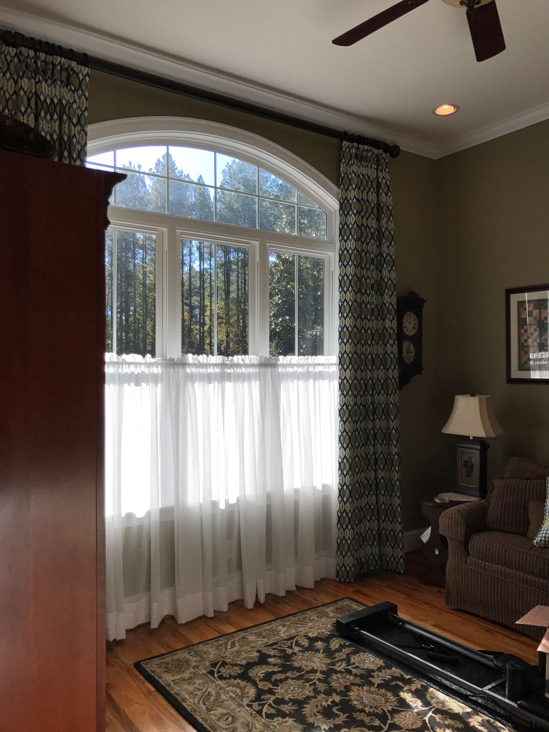 Living room with large arched window, sheer curtains, patterned rug, and armchair by a lamp