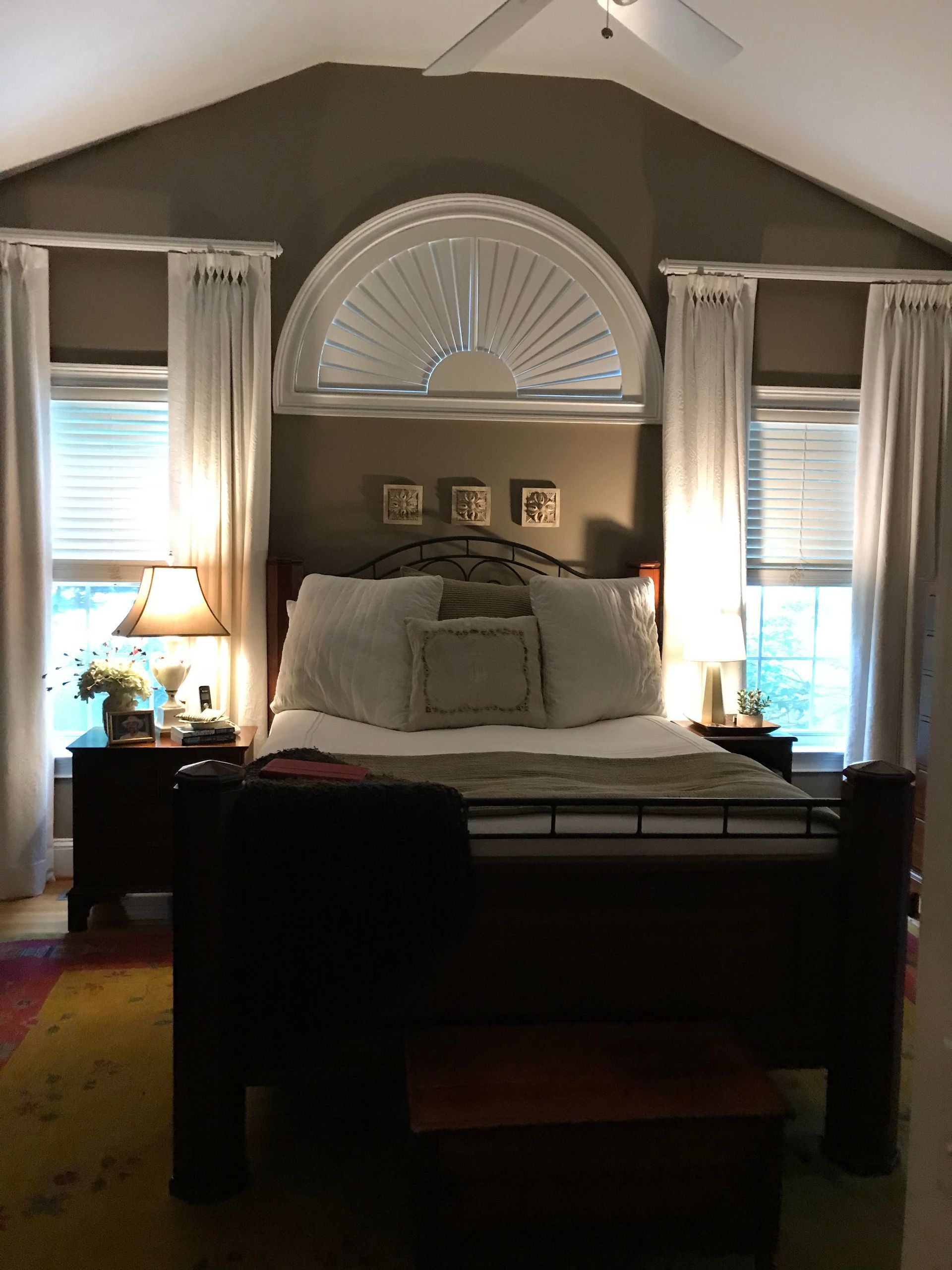 Bedroom with dark walls, white bedding, and arched window blinds lit by lamps on both sides of the bed