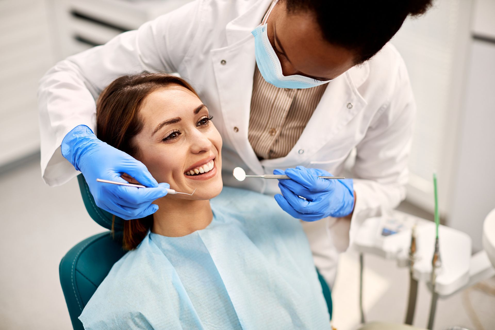 A woman is sitting in a dental chair while a dentist examines her teeth.
