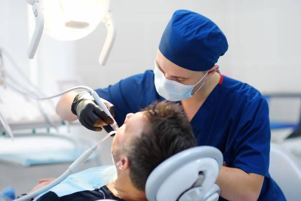 A dentist is examining a man 's teeth in a dental chair.