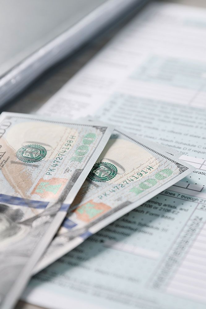Three $100 bills on tax forms next to a laptop.