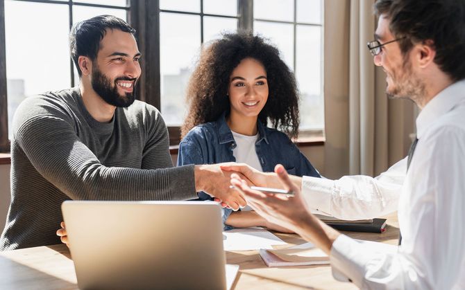 Couple shaking hands with a man at a table, smiling, likely a business meeting.