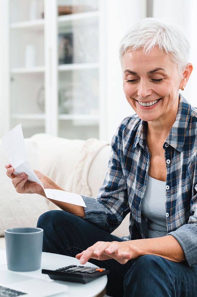 Woman smiling while calculating with a calculator, holding papers, and a coffee mug.