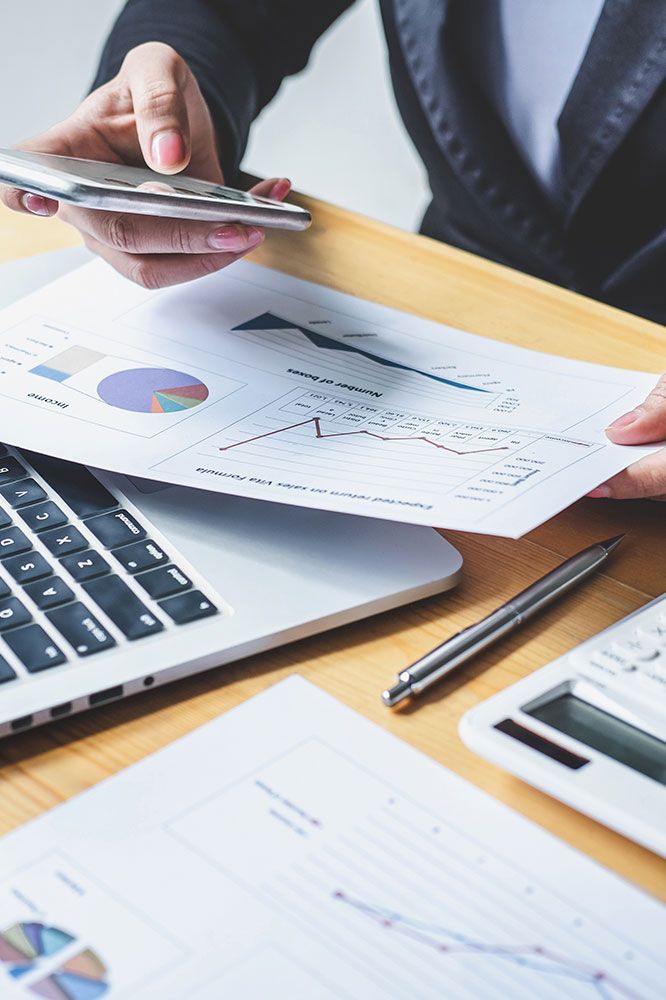 Person in suit examining charts and using a calculator and laptop at a desk.