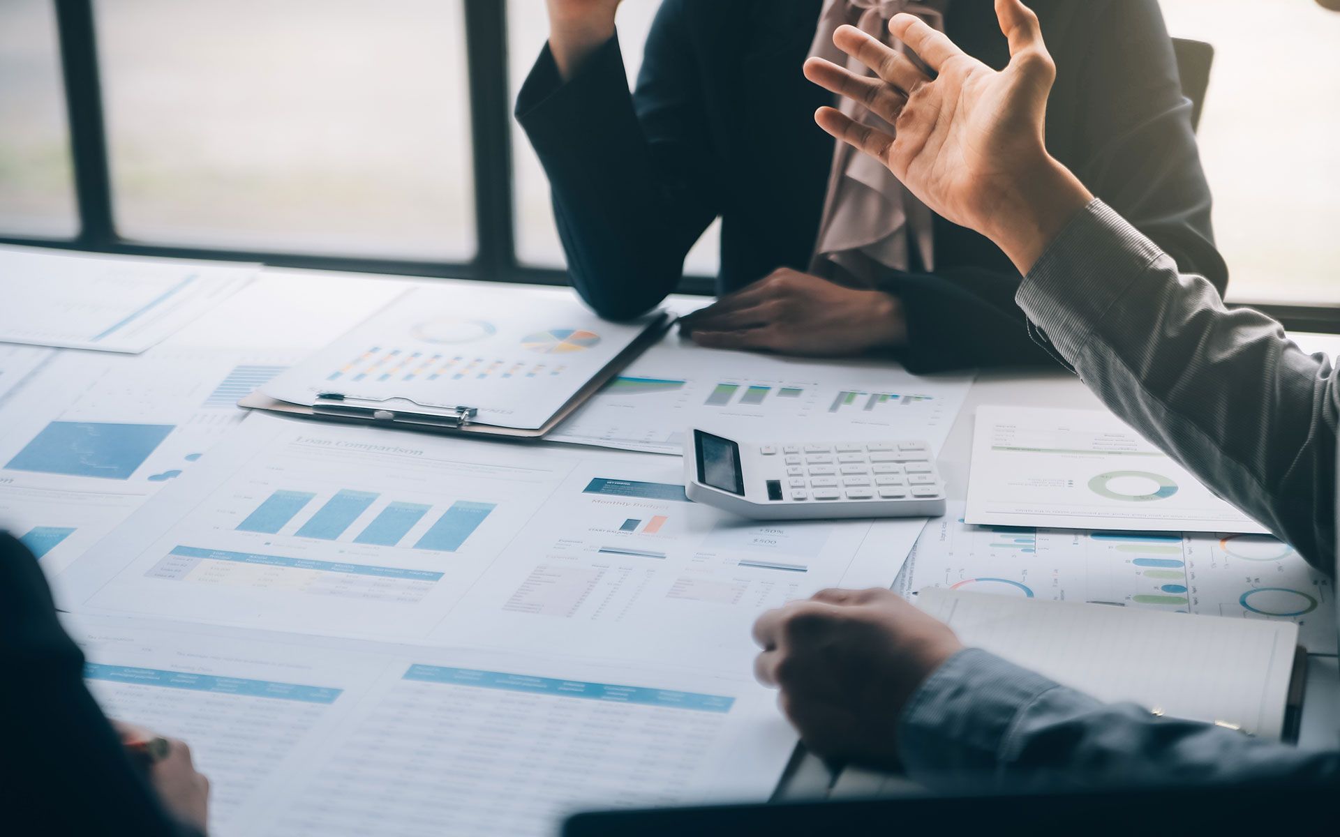 Business meeting with papers, charts, calculator, and hand gesturing over a table.