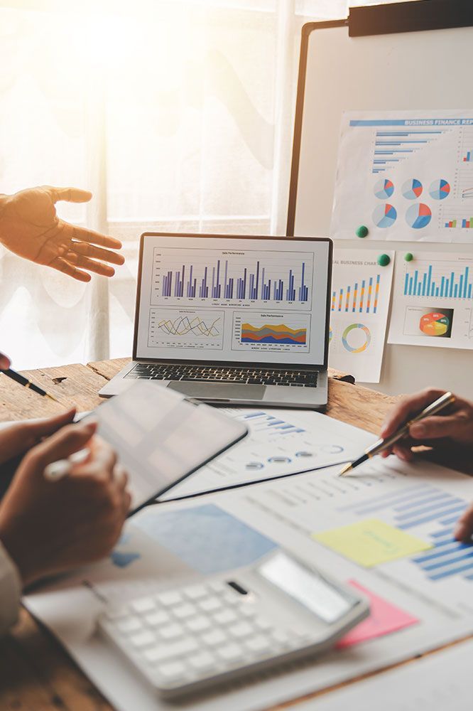 Business meeting with laptop displaying charts and graphs, papers, calculator, and two people pointing.