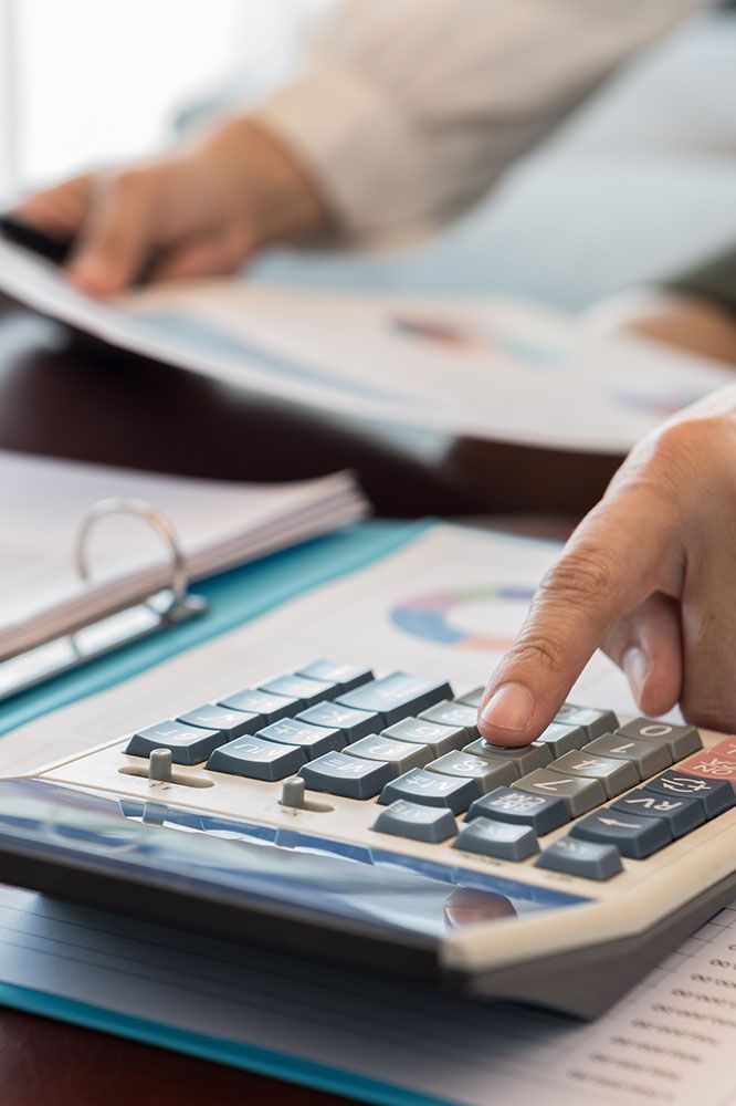 Person's hand using a calculator over financial documents with graphs and a binder.