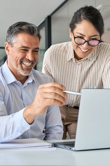Man and woman looking at laptop, both smiling. Man points at screen. Modern office setting.