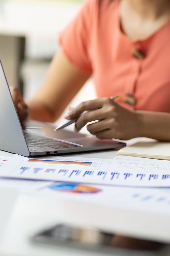 Person in orange top using laptop at desk with charts.