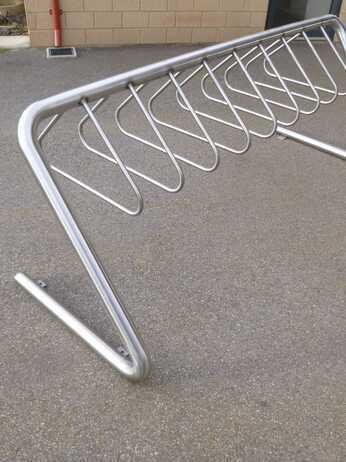 A stainless steel bike rack is sitting on the ground in a parking lot.