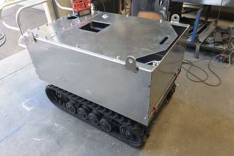 A metal box with tracks is sitting on a concrete floor.