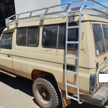 A tan van with a ladder on the back is parked on the side of the road.